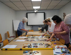 Frauen arbeiten gemeinsam mit Bildern an einem großen Tisch 
˜ Bildnachweis: © eventfive GmbH